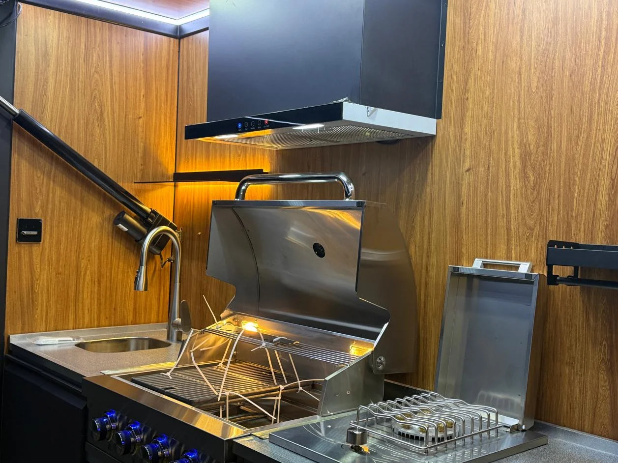 Kitchen interior with an open barbecue grill, range hood, sink and warm lighting